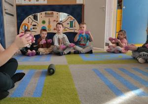 Dzieci obserwując nauczycielka wystukuja rytm na kubeczkach.