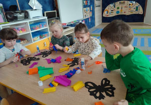 Dzieci wycinają nozyczkami bibułę i przyklejaja do szablonu motyla.