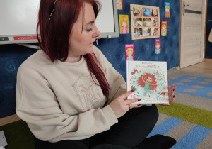 Nauczycielka prokazuje dzieciom książkę, którą im będzie czytać.