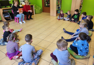 Dzieci siedzą na podłodze, słuchają książki.
