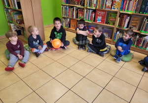 Dzieci siedzą na podłodze, podają piłkę.
