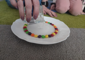 Nauczycielka wlewa powoli wodę do talerza z cukierkami.