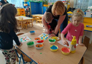 Dzieci gąbką tapuja kartkę farbą.