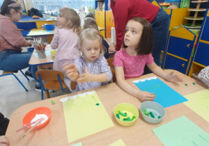 Dzieci pastelą zieloną rysują łodygę kwiatka.