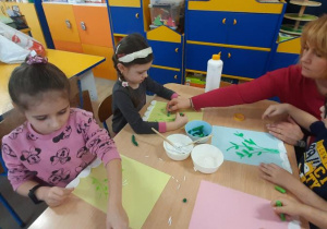 Dzieci pastelą zieloną rysują łodygę kwiatka i listki.