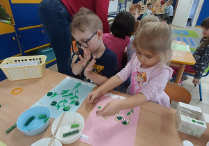 Dzieci doklejają patyczki do uszu do plasteliny zielonej.