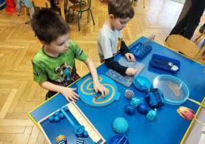 Dzieci bawią się przy stolikach z różnego rodzaju pomocami sensorycznymi.