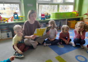 Dzieci słuchają książki czytanej przez nauczycielkę.