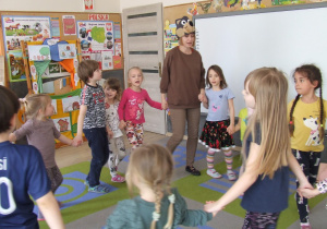 Dzieci tańczą w kole razem z nauczycielką ubraną w maskę wilka.