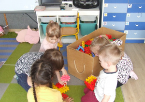 Dzieci budują domek z klocków plastikowych.