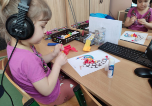 Dziewczynka wykleja obrazek kury kolorową bibułą.
