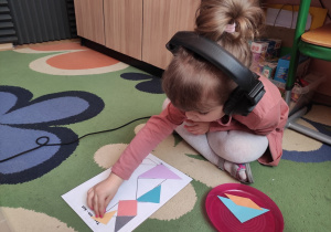 Dziewczynka układa tangram wykorzystując kolorowe figury geometryczne.