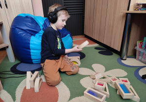 Chłopiec układa budowlę z dużych drewnianych klocków.