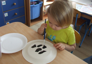 Dziewczynka robi łaty z czarnej farby na papierowym talerzu.