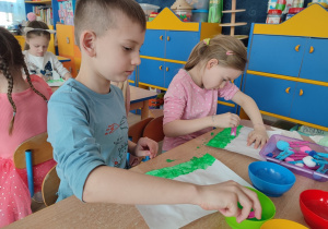 Dzieci malują spinaczem z watą namoczonym w farbie po kartce.