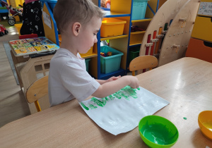 Chłopiec maluje palcem pom kartce.