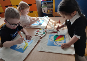 Dzieci na torbach z materiałuy malują farbami korzystując szablonów.