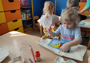 Dziewczynka maluje przykłada szablon do torby i maluje wzór.