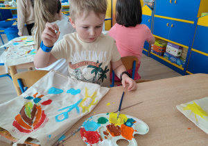 Chłopiec maluje farbami na swojej torbie.