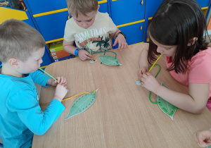 Dzieci uzywając słomki łapią robale leżące na stole.