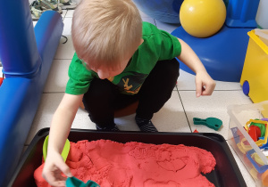 Chłopiec siedzi i odciska kształty w piasku kinetycznym.