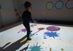 Chłopiec tworzy kolorowe plamy na podłodze interaktywnej.