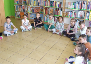 Dzieci siedzą w półkolu i słuchają czytanej książki.