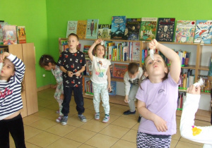 Dzieci wykonują ćwiczenia oddechowe - dmuchają w piórka tak, aby nie spadły na podłogę.