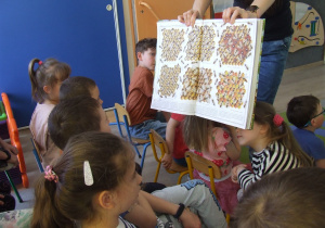 Dzieci oglądają ilustracje z książki, jak wygląda praca pszczół w ulu.
