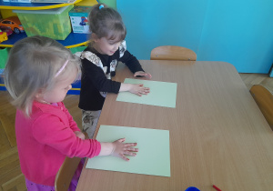 Dziewczynki odbijają swoją dłoń na kartce papieru.