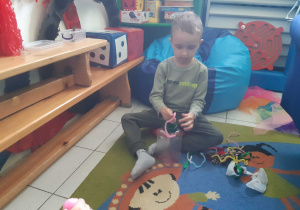 Chłopiec siedzi na dysku sensorycznym i układa druciki kreatywne.