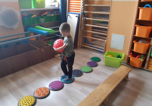 Chłopiec trzyma piłkę piankową i idzie po wyspach sensorycznych.