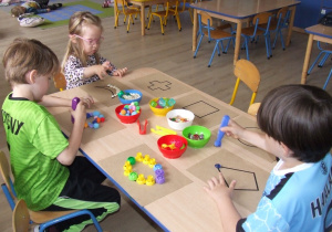 Dzieci układają wzory na papierze wykorzystując pompony, korki, fasolę.