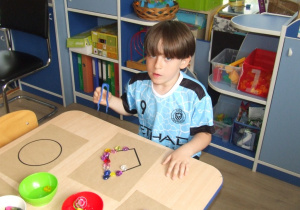 Chłopiec układa wzór na papierze wykorzystując kolorowe kryształki.