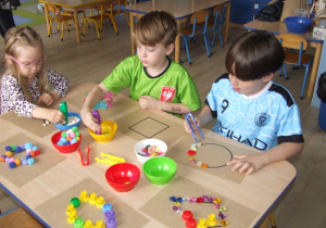 Dzieci układają wzory na papierze wykorzystując guziki, korki, fasolę.