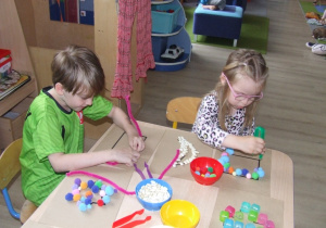 Dzieci układają wzory na papierze wykorzystując kolorowe pompony i druciki..