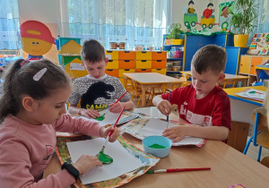 Dzieci malują zieloną farbą liść bzu.