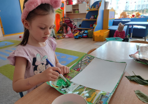 Dziewczynka maluje farbą liść bzu.