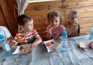 Dzieci jedzą kiełbaski z grila.
