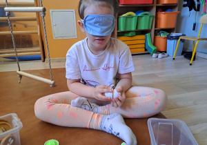 Dziewczynka z zasłoniętymi oczami siedzi na materacu i układa.