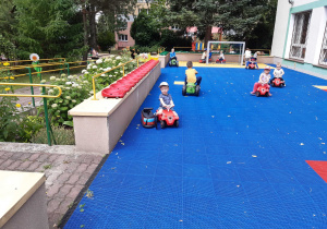 Dzieci jeżdżą na samochodzikach ogrodowych po tarasie przedszkolnym.
