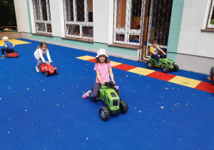 Dzieci jeżdżą na samochodzikach ogrodowych po tarasie przedszkolnym.