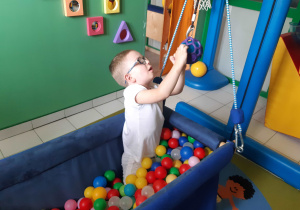 Chłopiec w podwieszanym basenie z kulkami wkłada chusteczkę do kulki.