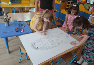 Dzieci w małych grupach malują farbami postać.