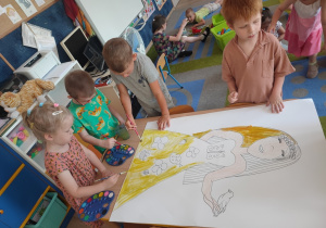 Dzieci w małych grupach malują farbami postać.