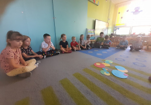 Dzieci siedzą na dywanie i patrzą na kolorowe kropki.
