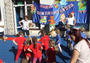 Dzieci tańczą na tarasie przedszkolnym według instrukcji pokazywanej przez nauczycielki.