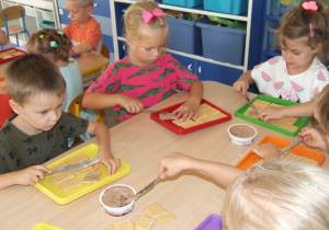 Dzieci smarują herbatniki serkami - czekoladowym i waniliowym.