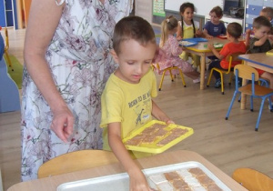 Chłopiec z pomocą nauczycielki układa ciastka na dużych tacach - układa je we wzór zebry.