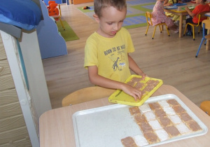 Chłopiec układa ciastka na dużych tacach - układa je we wzór zebry.
